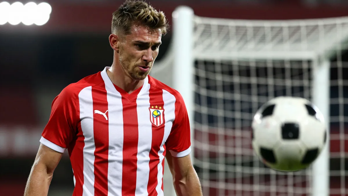 A young male football player in a red and white striped jersey, mid-20s, muscular build, midfielder, frustration on his...